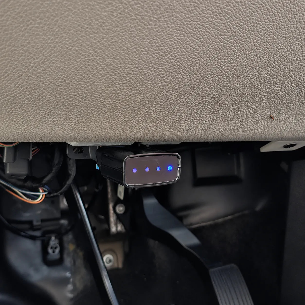 Close-up view of the MOQWAIG AFM DFM disabler installed in a vehicle OBD-II port with blue lights showing active connection.